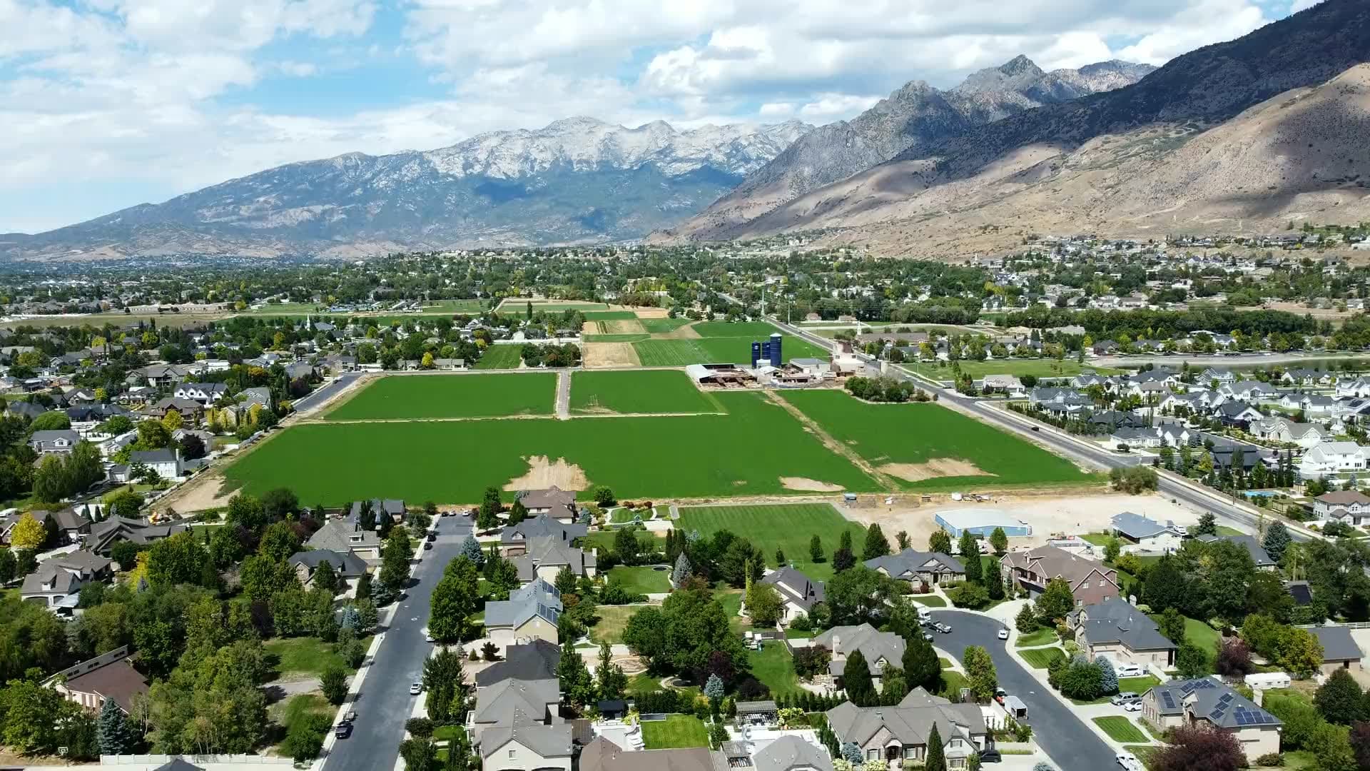 Aerial view of Utah Valley on a summer afternoon — green fields and neighborhoods beneath Mount Timpanogos