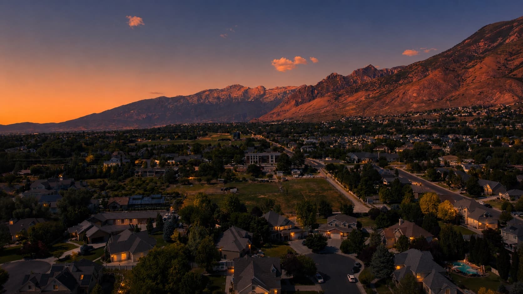A Utah County neighborhood at dusk with warm-lit homes and the Wasatch range in alpenglow