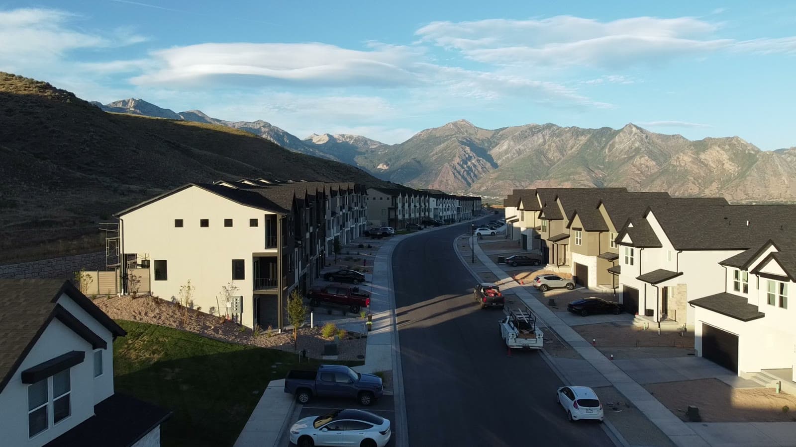 Golden-hour view down an Inverness street in Lehi, townhomes and single-family homes with the Wasatch peaks rising at the end of the block