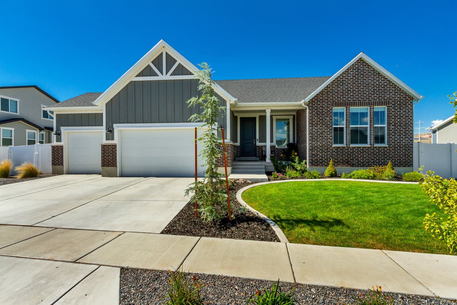 Front of the home from the driveway: brick and gray siding, covered porch, and a three-car garage
