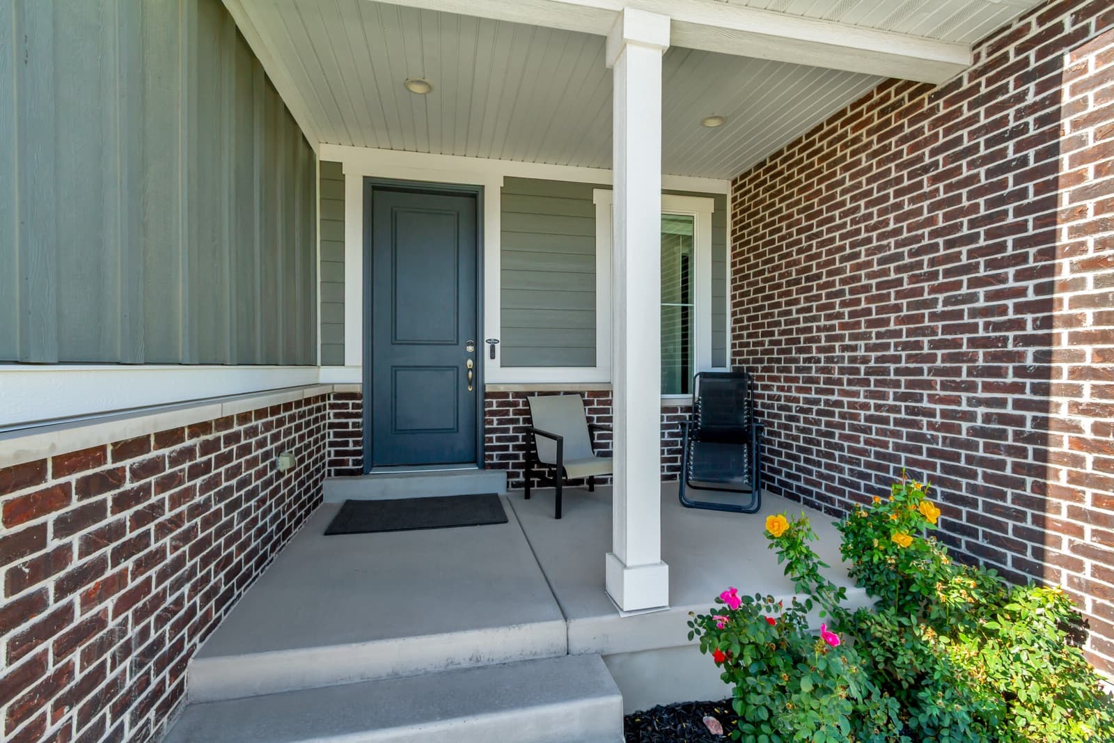 Covered front porch with brick, a white column, and the front door