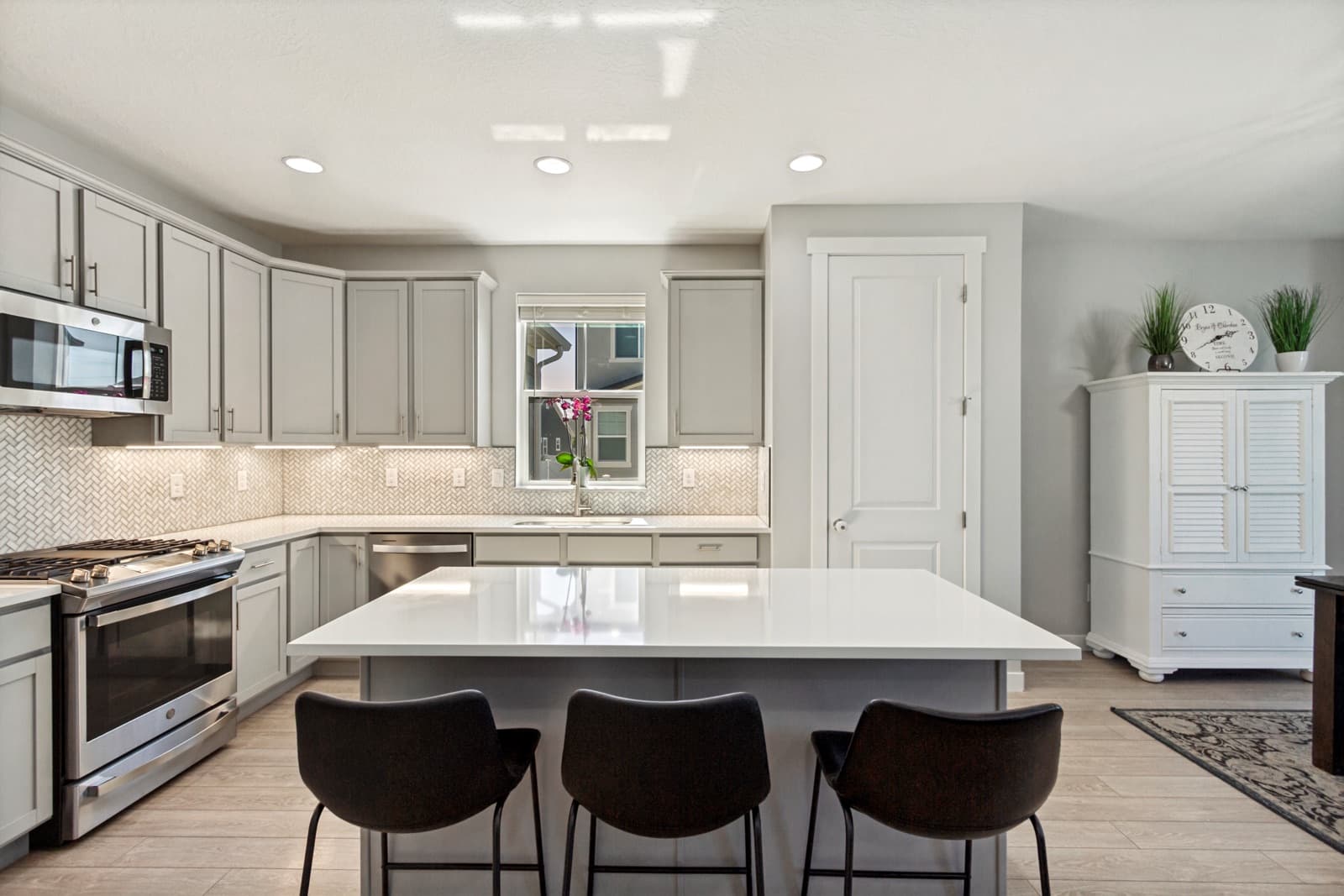 Kitchen with gray cabinets, a white quartz island with three stools, and a gas range