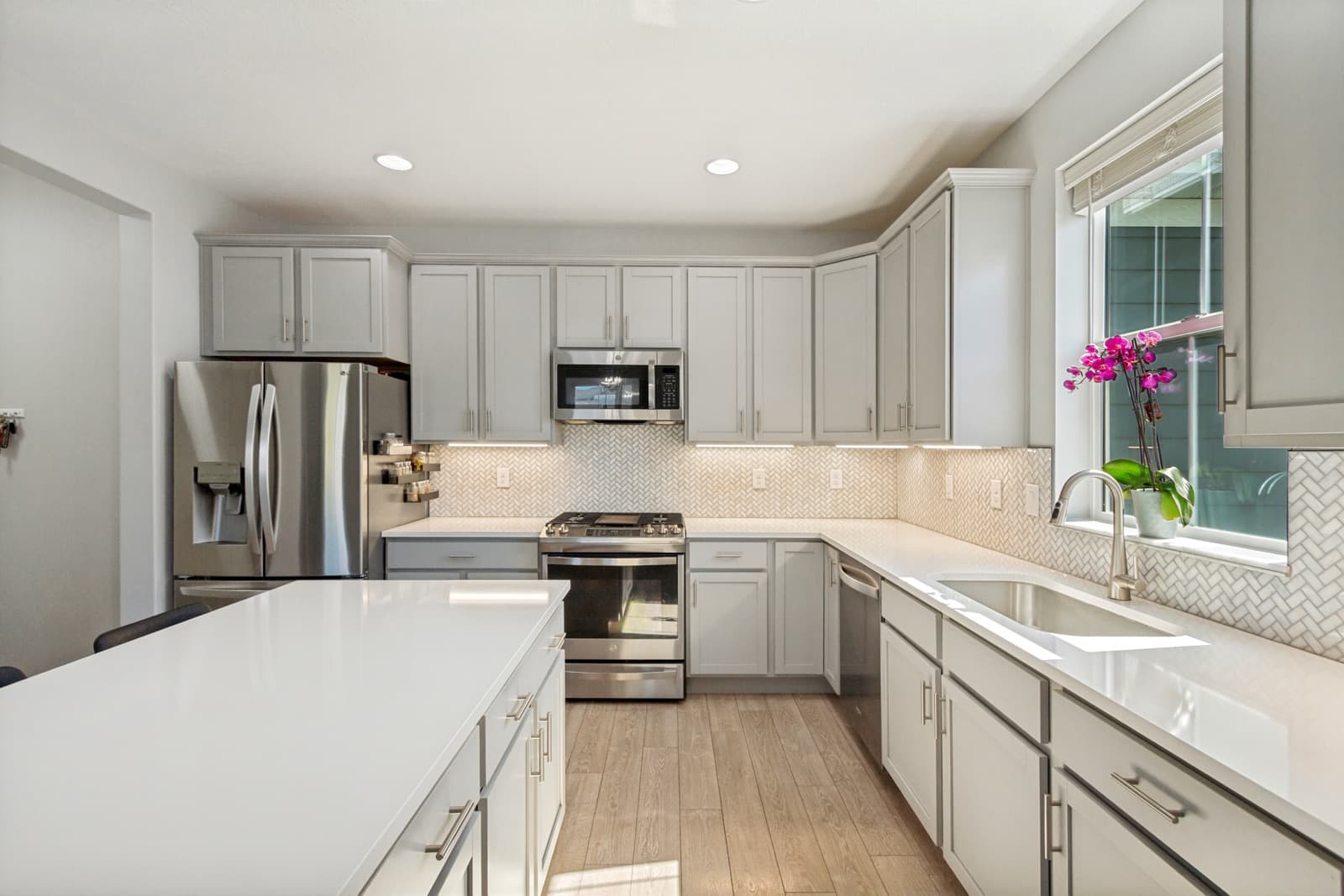 Kitchen sink under a window with a herringbone backsplash and stainless appliances