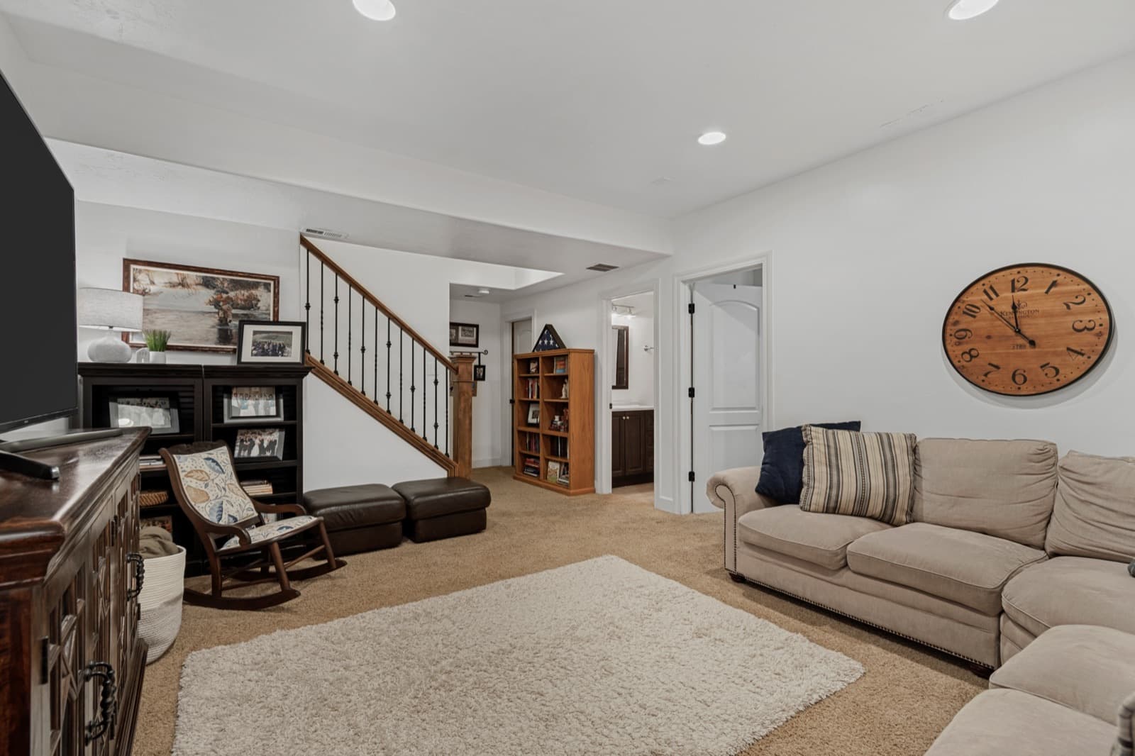 Lower-level family room seen from the basement stairs, carpeted with recessed lighting