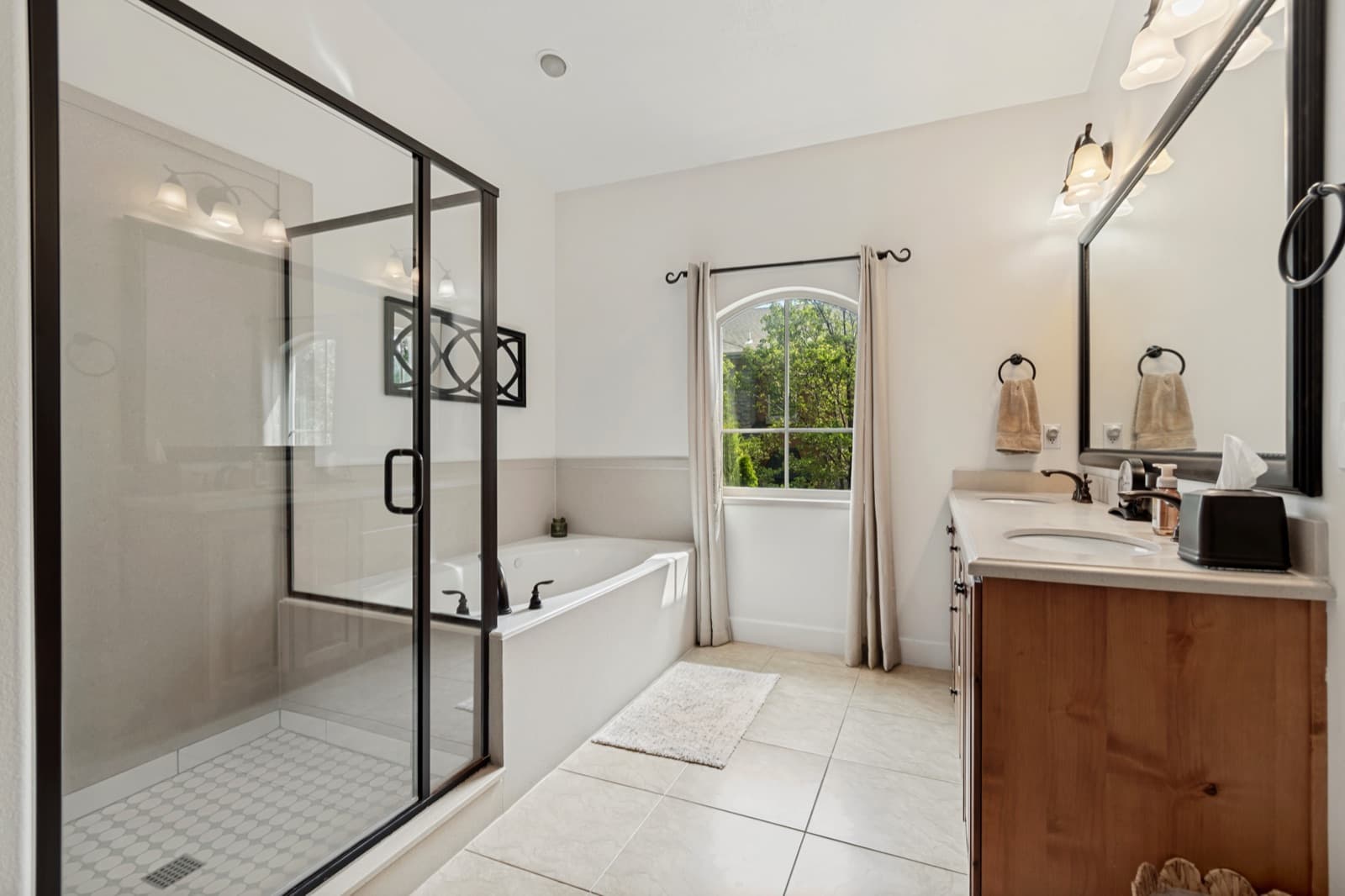 Primary bathroom with a glass-door shower, corner soaking tub, wood vanity, and arched window