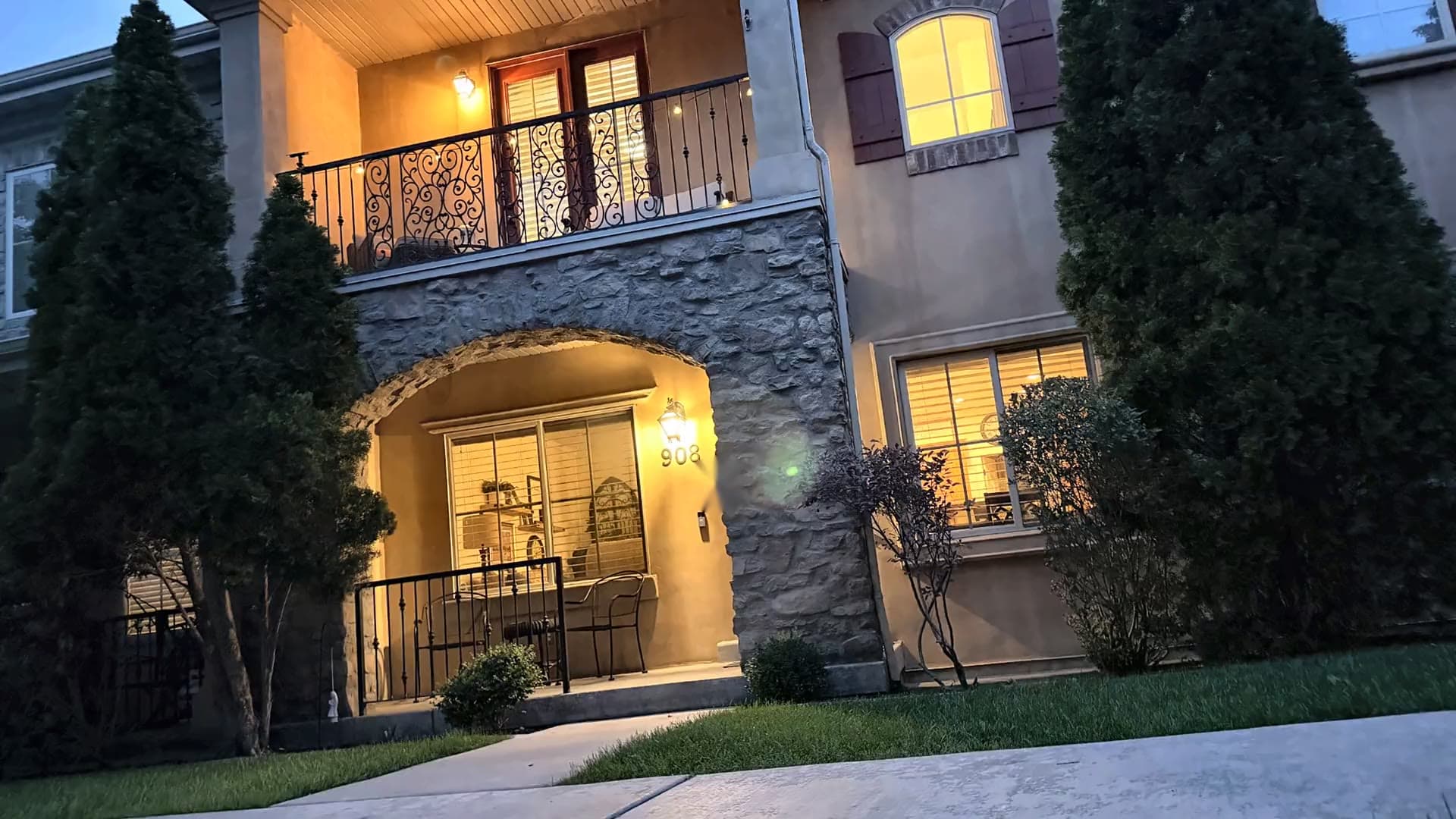 908 N 940 W in Orem at twilight — stone arched entry with the covered balcony above, lights on inside