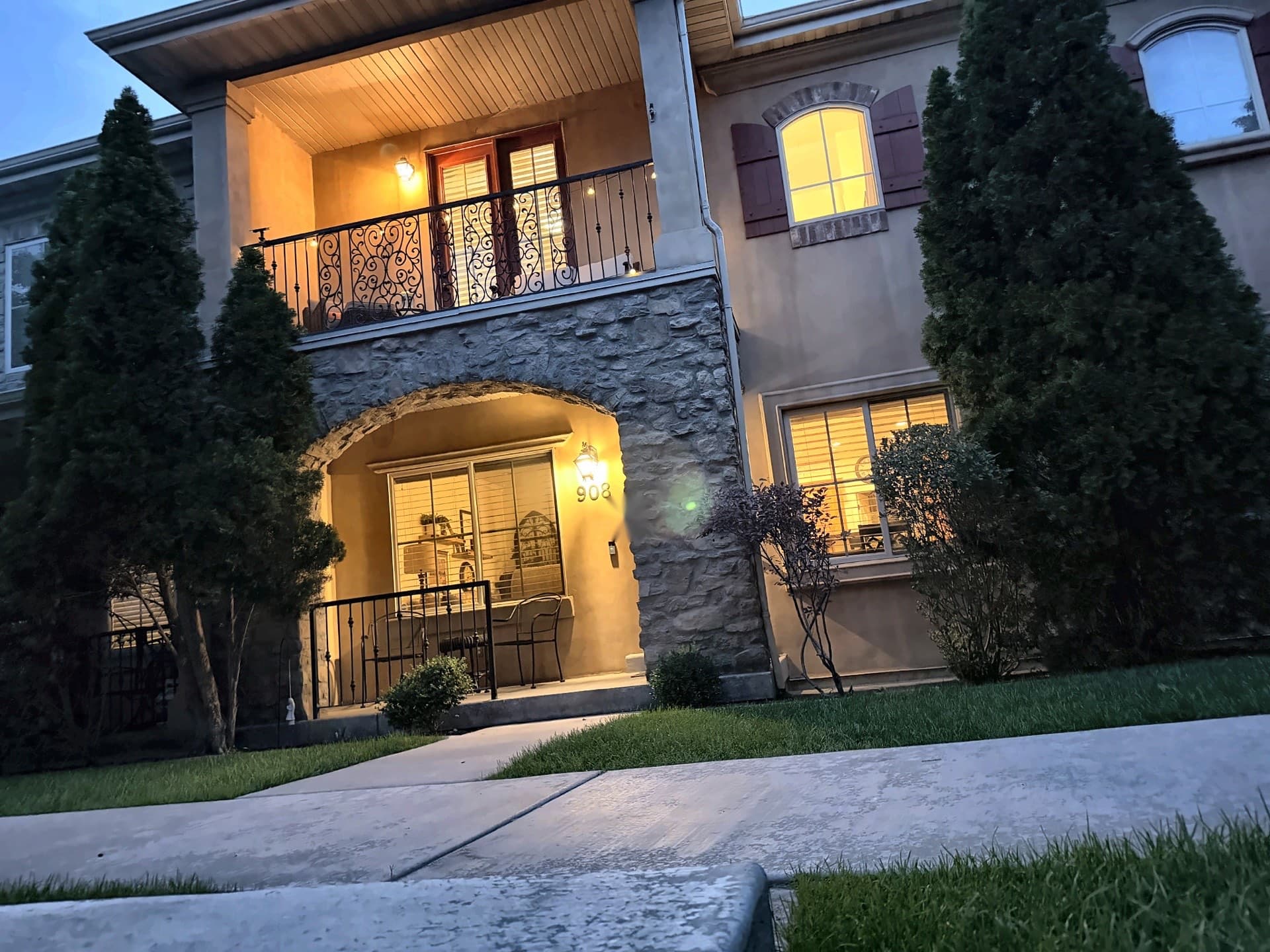 908 N 940 W in Orem at twilight — stone arched entry with the covered balcony above, lights on inside